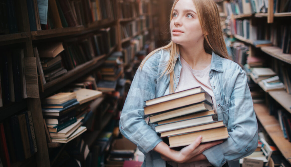 A Small Girl Standing In A Big Old Book Store And Holding Many B