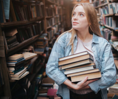 A Small Girl Standing In A Big Old Book Store And Holding Many B